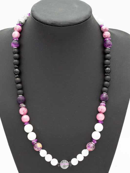 A handcrafted gemstone necklace displayed on a black bust, featuring a stunning gradient of crystal beads representing the chakras. The arrangement transitions from deep grounding black stones at the base, through fiery reds, golden yellows, and lush greens, to calming blues and purples at the crown. Each bead is carefully selected to resonate with its corresponding chakra, promoting balance and energetic flow.