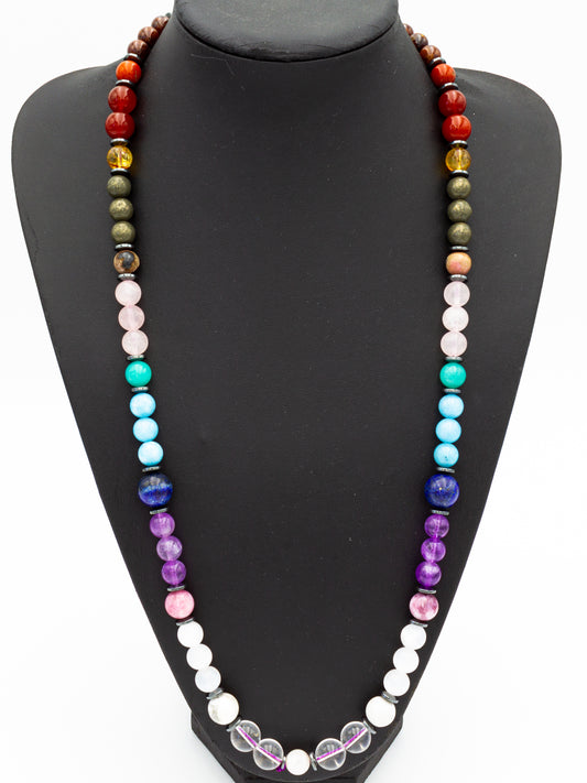 A vibrant chakra necklace crafted from an array of natural gemstones, each bead corresponding to the energy centers of the body. The arrangement flows from deep grounding tones of black and red at the base, rising through golden, green, and blue hues, culminating in luminous white and violet stones at the crown. This sacred adornment serves as a conduit for energetic balance, spiritual connection, and personal empowerment, harmonizing the wearer's vibrational field.