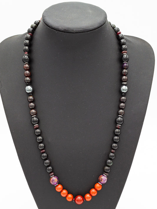 A handcrafted gemstone necklace featuring a vibrant array of polished beads, each aligned to channel specific energies. Rich hues of deep black obsidian, grounding hematite, and fiery red jasper create a striking contrast, while dark garnet and shimmering amethyst enhance the piece’s metaphysical resonance. The necklace exudes an aura of strength, balance, and spiritual harmony, making it both a protective talisman and a statement of empowerment.